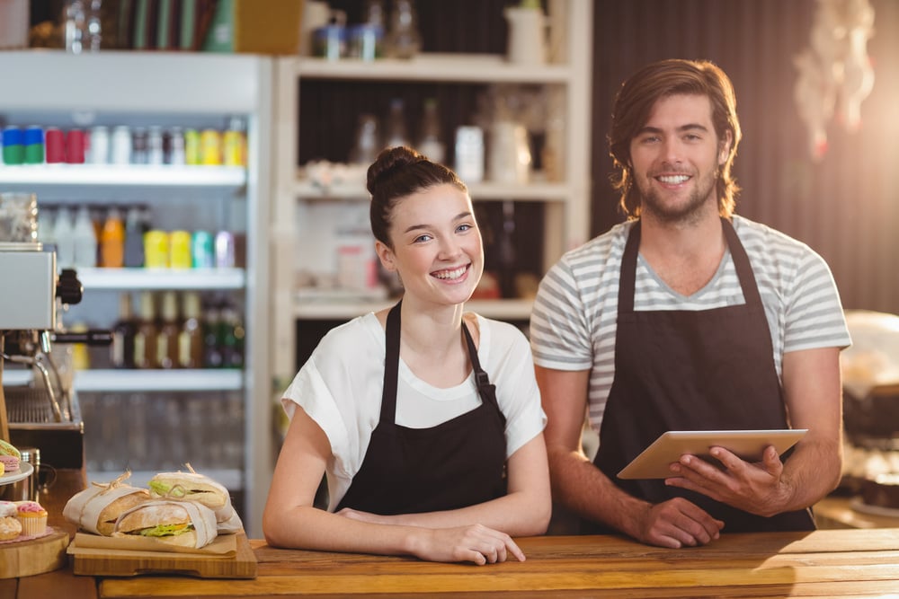 Smiling waiter and waitress using digital tablet at counter in cafe